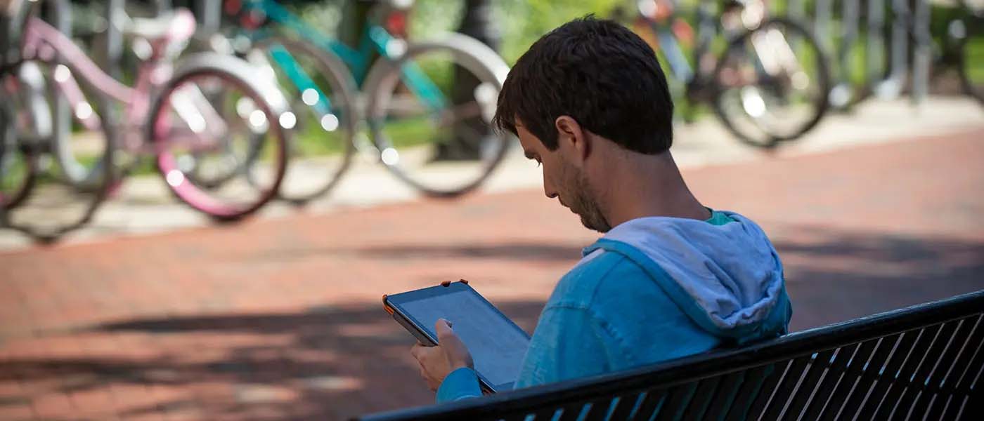 a v.c.u. student sits on a bench reading a tablet device